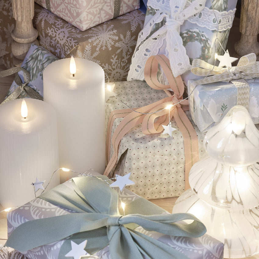 Geschenke und Lichterkette mit Holzsternen auf einem Sessel, davor ein Dekozweig mit Eicheln und Tannenzapfen