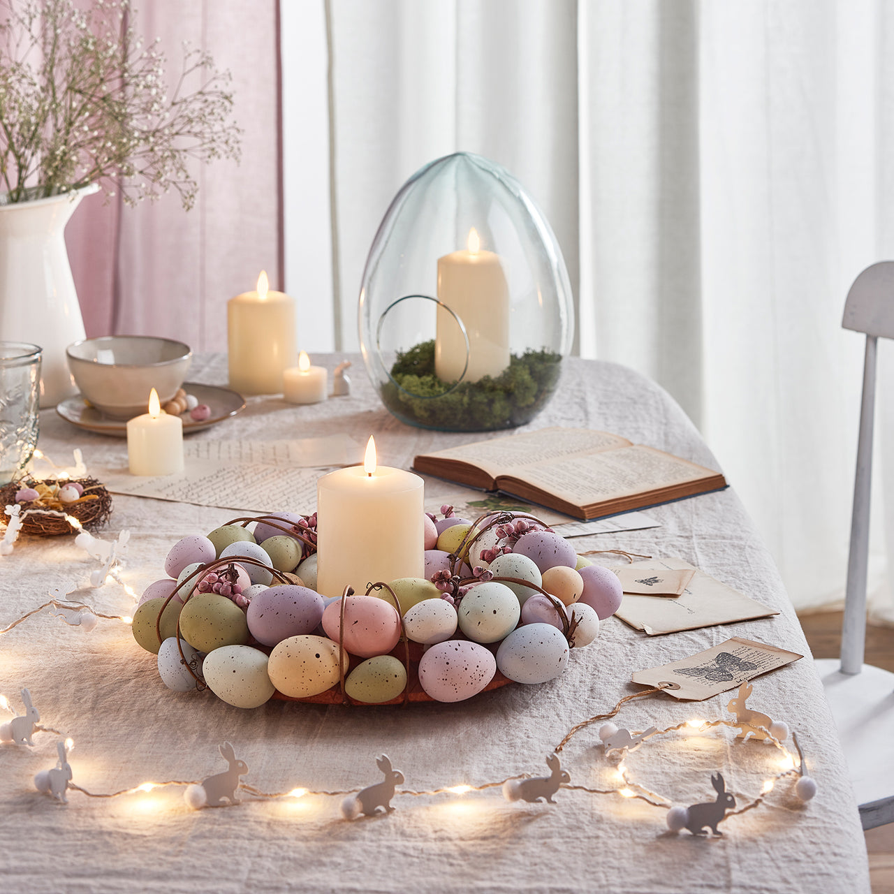 Osterdeko auf Tisch mit Hasen Lichterkette, Osterei Vase, Kerzen und Osterei Kranz.