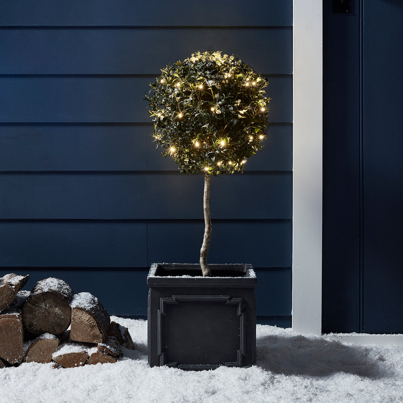 Kleiner Baum mit warmweißer Lichterkette im Schnee.