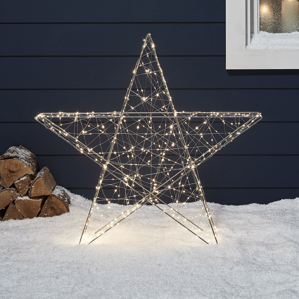 Micro-LED-Stern im Schnee vor blauer Hauswand.