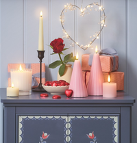 Für den Valentinstag in Rosatönen dekoriertes Sideboard mit LED Kerzen, Herzlichterkette, LED Herz, Luftballons und Prosecco