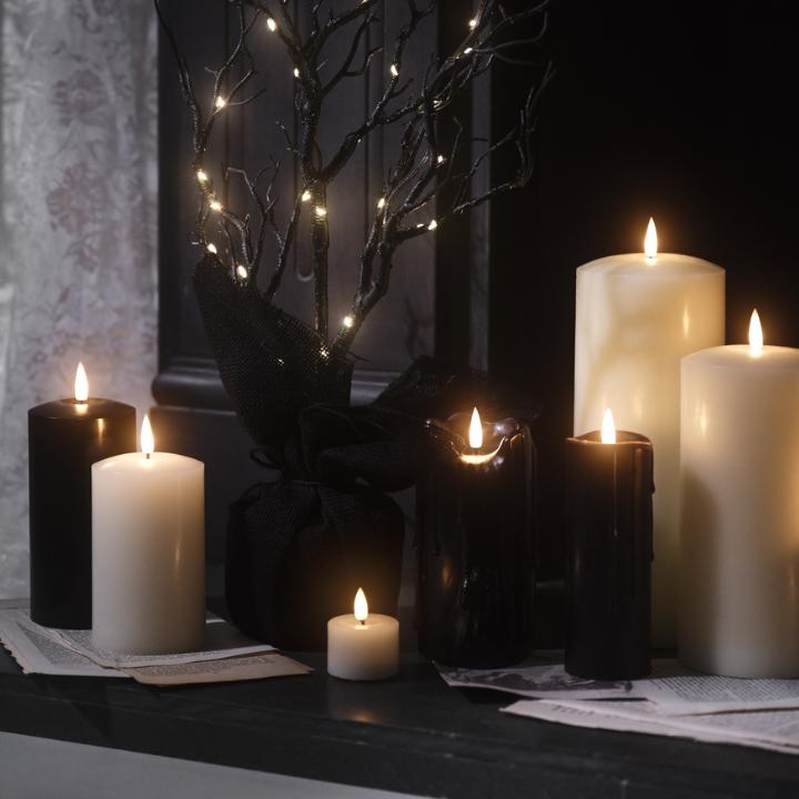 Schwarze LED Kerzen und Halloween-Laterne mit Hexenmotiv auf einer Holzkommode
