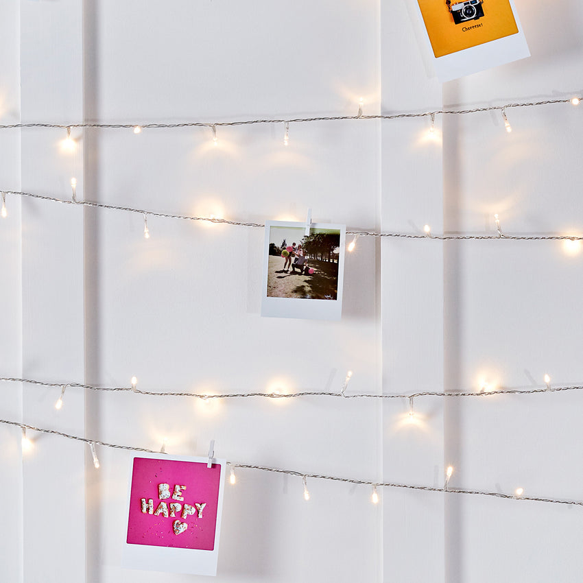An einer weißen Wand drapierte warmweiße Lichterkette mit angepinnten Postkarten