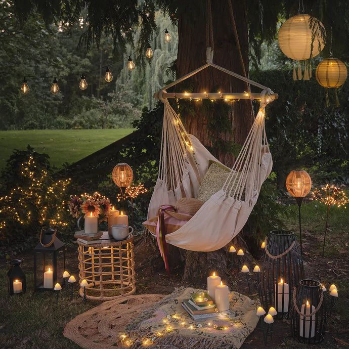 Gemütlicher Garten mit Hängesessel, Laternen und warm leuchtenden Solarleuchten am Abend