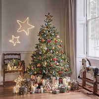 Geschenke und Lichterkette mit Holzsternen auf einem Sessel, davor ein Dekozweig mit Eicheln und Tannenzapfen