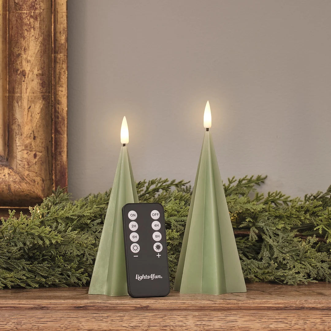 Zwei grüne LED-Spitzkerzen mit Fernbedienung (lights4fun-Branding), warmweiße brennende Flammen, Tannenzweige-Dekoration auf Holz, Timer-Funktionen sichtbar.