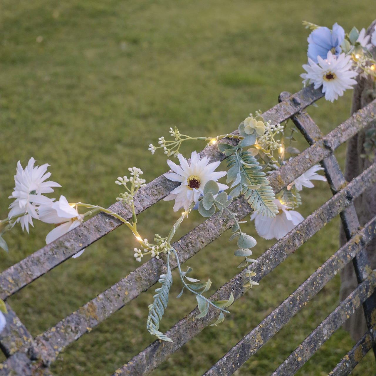 Beleuchteter Kranz und Girlande mit blauen und weißen Blüten auf Bank draussen