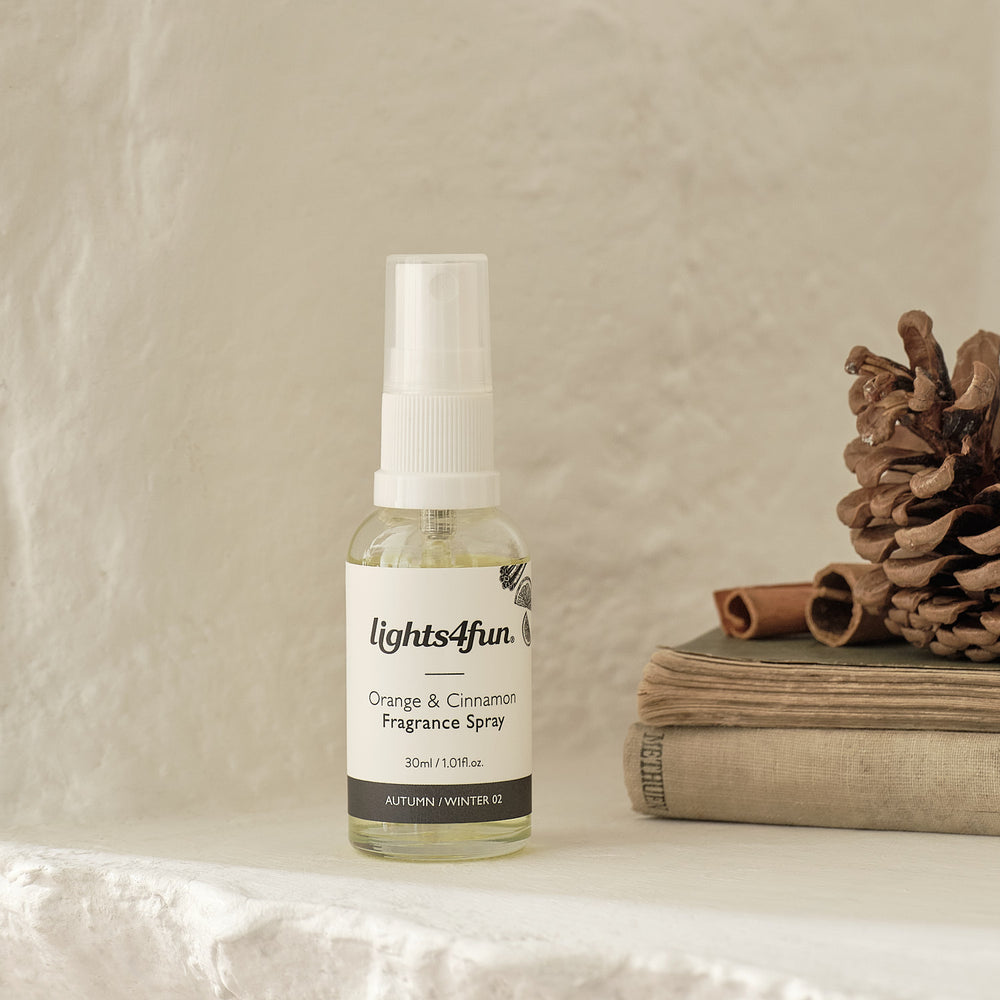 Nahaufnahme einer lights4fun Raumduft-Spray-Flasche mit botanischem Etikett und Premium-Verpackung, arrangiert auf gestapelten Leinentüchern mit braunen Pinienzapfen und natürlichen Holzdekorationen – luxuriöses Duftspray für wohnliche Raumaromatisierung mit eleganter Produktpräsentation und hochwertiger Verpackungsästhetik.