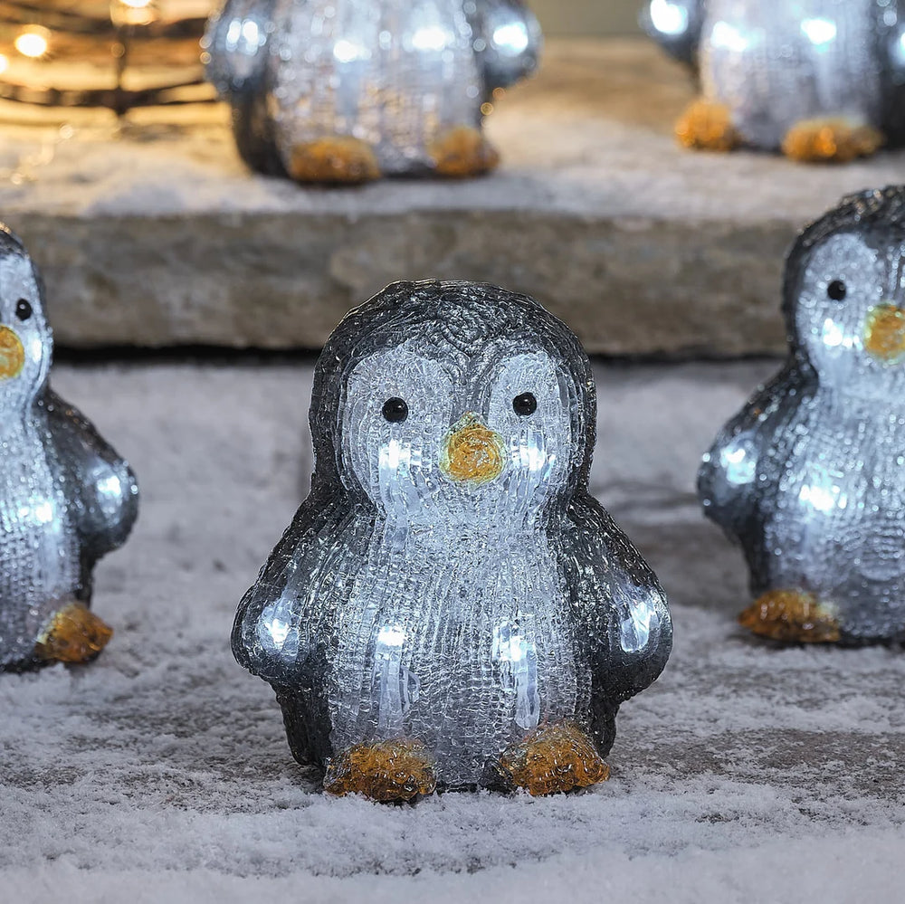 Niedliche glitzernde Pinguin-Dekofigur mit grauem Schneeeffekt-Finish, goldenen Akzenten und weißen Augen, positioniert auf Stein-Untergrund mit unscharfem Hintergrund – festliche Weihnachtsfigur für Außendekoration, Garten-Arrangements und winterliche Hausdekorationen mit charmanter Schneekristall-Textur.