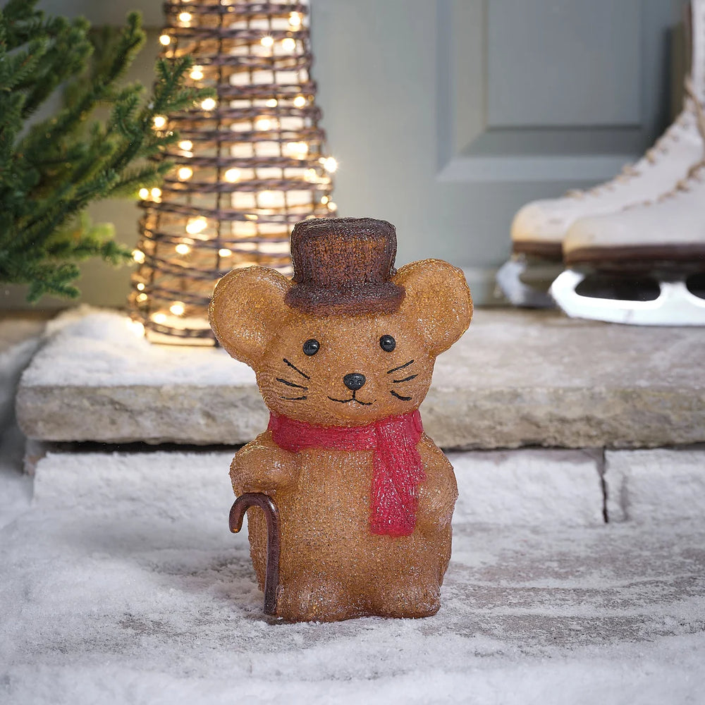 Niedliche glitzernde hellbraune Maus-Dekofigur mit feinen Weihnachtsakzenten und strukturiertem Glitter-Finish, arrangiert auf Schneeuntergrund vor winterlichem grünem Hintergrund – liebevolle Plüschfigur für klassische Weihnachtsarrangements und festliche Außendekoration mit warmem Charme.