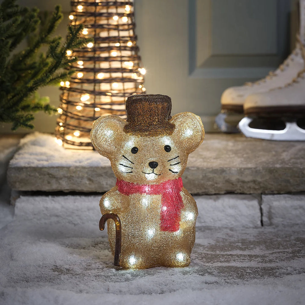 Charmante glitzernde goldene Maus-Dekofigur mit roter Weihnachtsschleife, positioniert vor beleuchteter Kegel-Weihnachtsbaumdekoration auf Stein-Terrasse – festliche Plüschfigur für Außendekoration, Garten-Arrangements und weihnachtliche Hausdekorationen mit eleganter Glitter-Textur und warmweißer LED-Beleuchtung im Hintergrund.