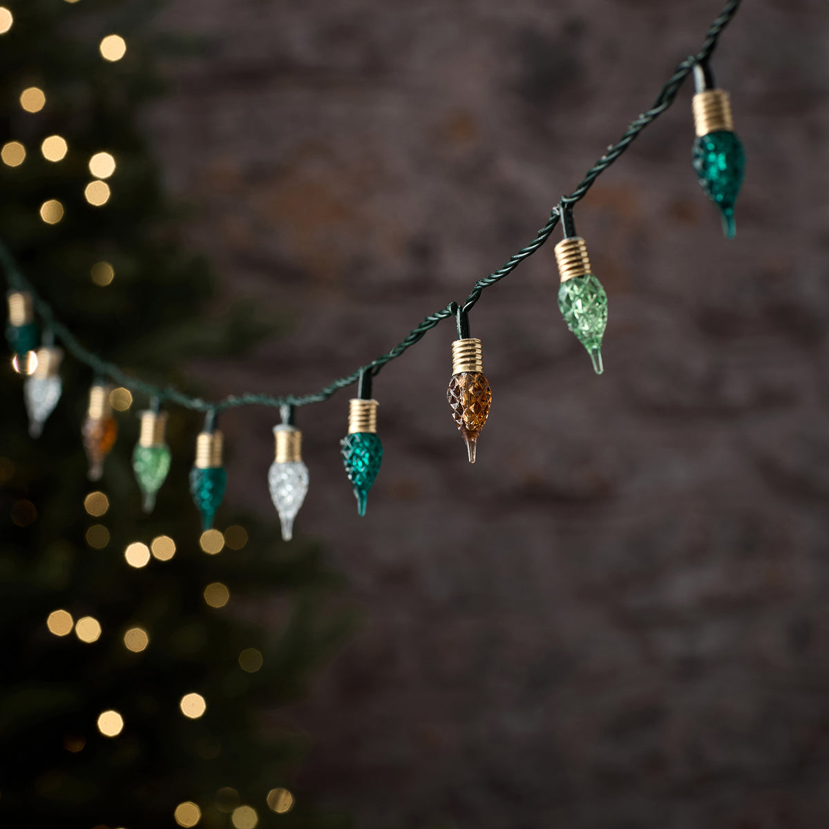 Premium-LED-Lichterkette mit schwarzem Draht und hängenden Tropfen-Anhängern in Regenbogenfarben (Grün, Gold, Orange, Weiß), arrangiert vor unscharfem Bokeh-Lichthintergrund – dekorative mehrfarbige Lichterkette für elegante Außen-Weihnachtsarrangements und gehobene Fassaden-Dekorationen.