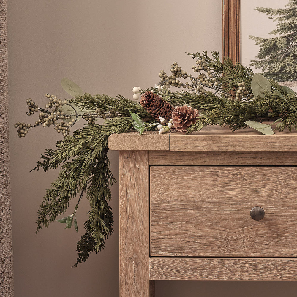 Stilvolles Fensterbrett-Arrangement mit dichtem grünem Fichtengrün, burgundy Blütenakzenten, weißen Beeren und natürlicher Textur, arrangiert auf cremefarbener Holzkommode vor Fenster mit eleganter Weihnachts-Dekoration – liebevolle Weihnachts-Tischdekoration für klassische Fensterdekorationen und gehobene Wohnzimmer-Arrangements.