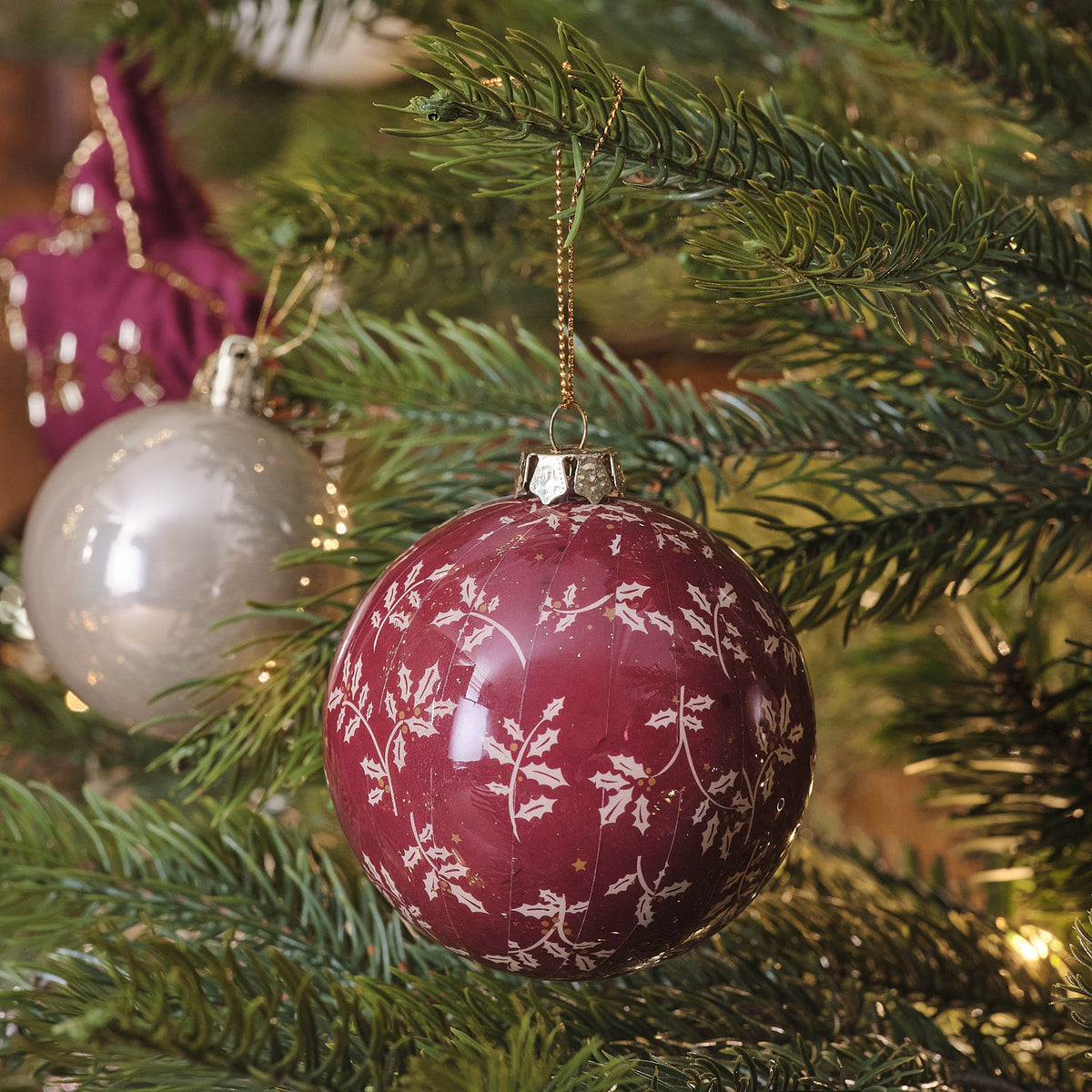 Perlweiße und rote Weihnachtskugeln am Tannenzweig mit violetter Schleife.