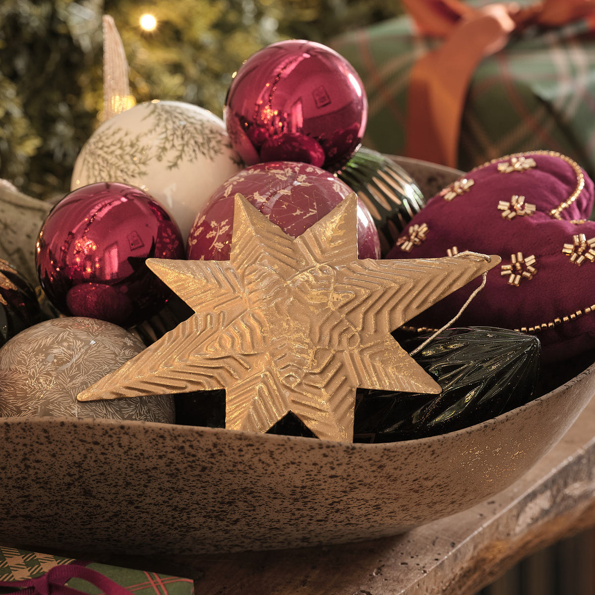 Holzschale mit bordeauxroten Weihnachtskugeln und goldenem Sternanhänger.