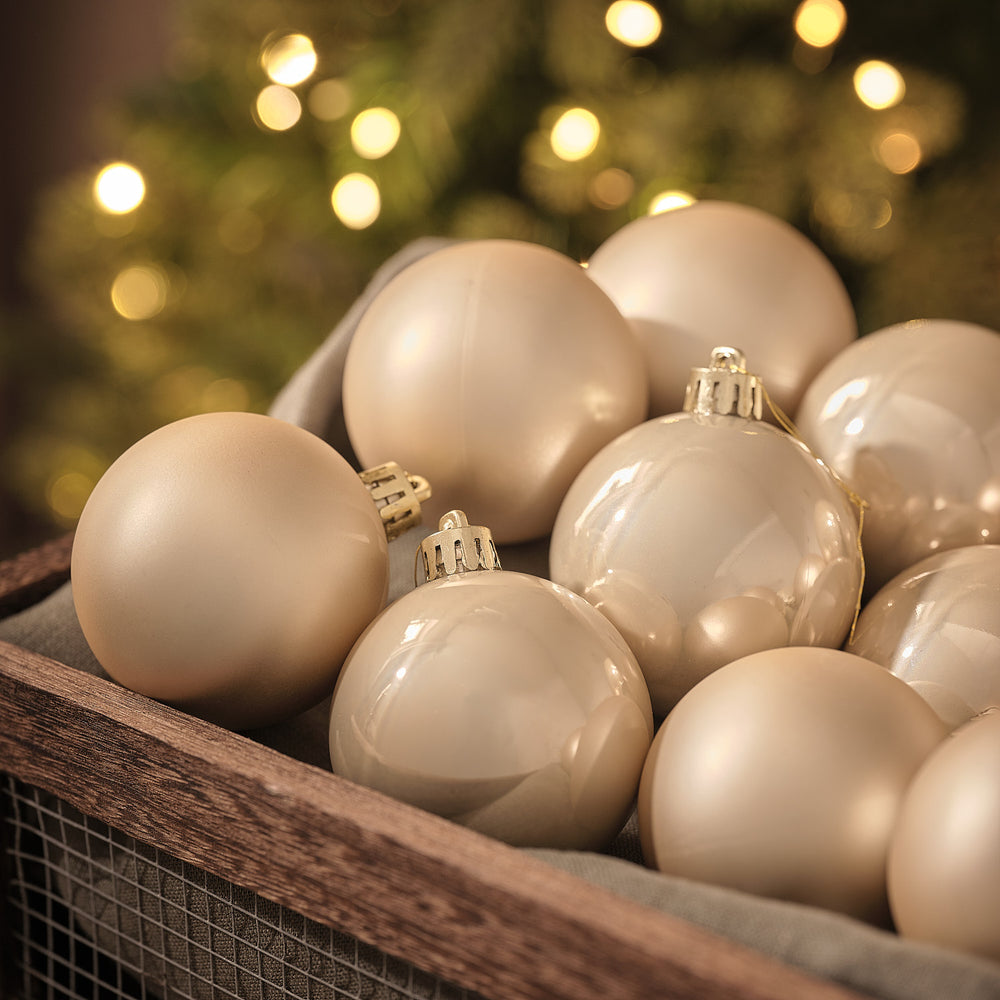 Champagnerfarbene Weihnachtskugeln in glänzender Optik in Holzkiste vor Lichterglanz.