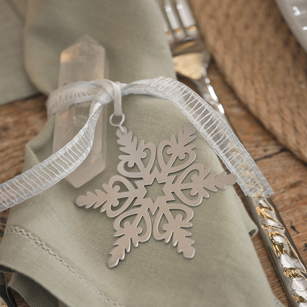Weißer Schneeflocken-Anhänger als Geschenkanhänger an Serviette mit Schleife.