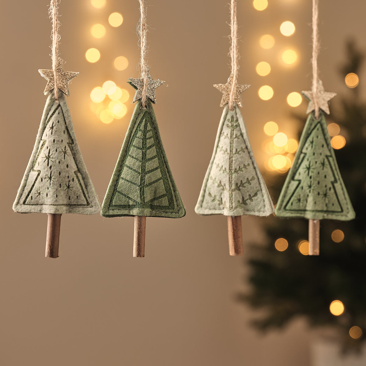 Grüne Stoff-Tannenbaum-Anhänger mit gesticktem Muster, Sternspitze und Holzsockel, hängend vor Lichterglanz.