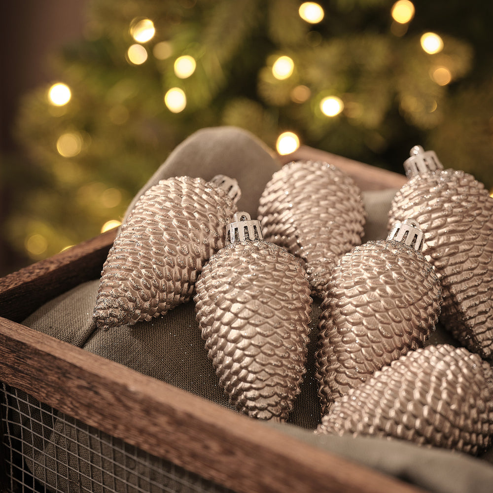 Tannenzapfen-Weihnachtskugeln in Holzkiste vor beleuchtetem Tannenbaum.