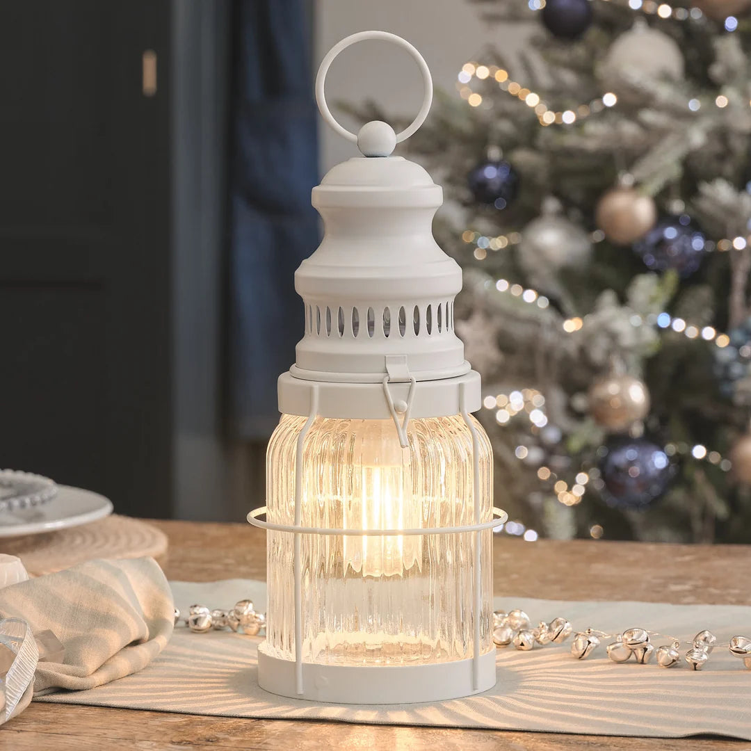 Weiße LED-Laterne mit Riffelglas auf winterlich dekoriertem Tisch vor Weihnachtsbaum.