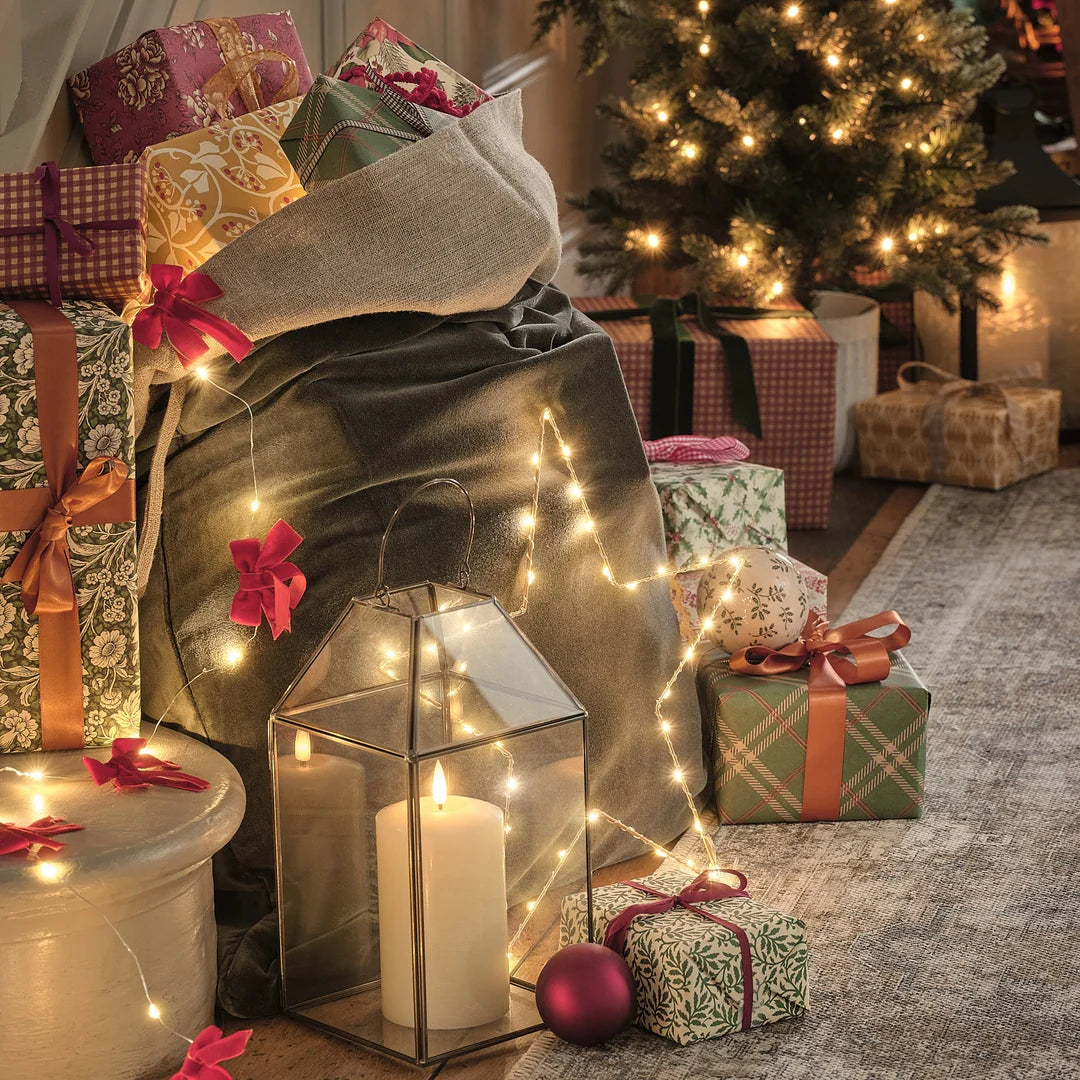 Goldene Metall-Laterne neben Geschenken und Weihnachtsbaum mit Lichterkette.