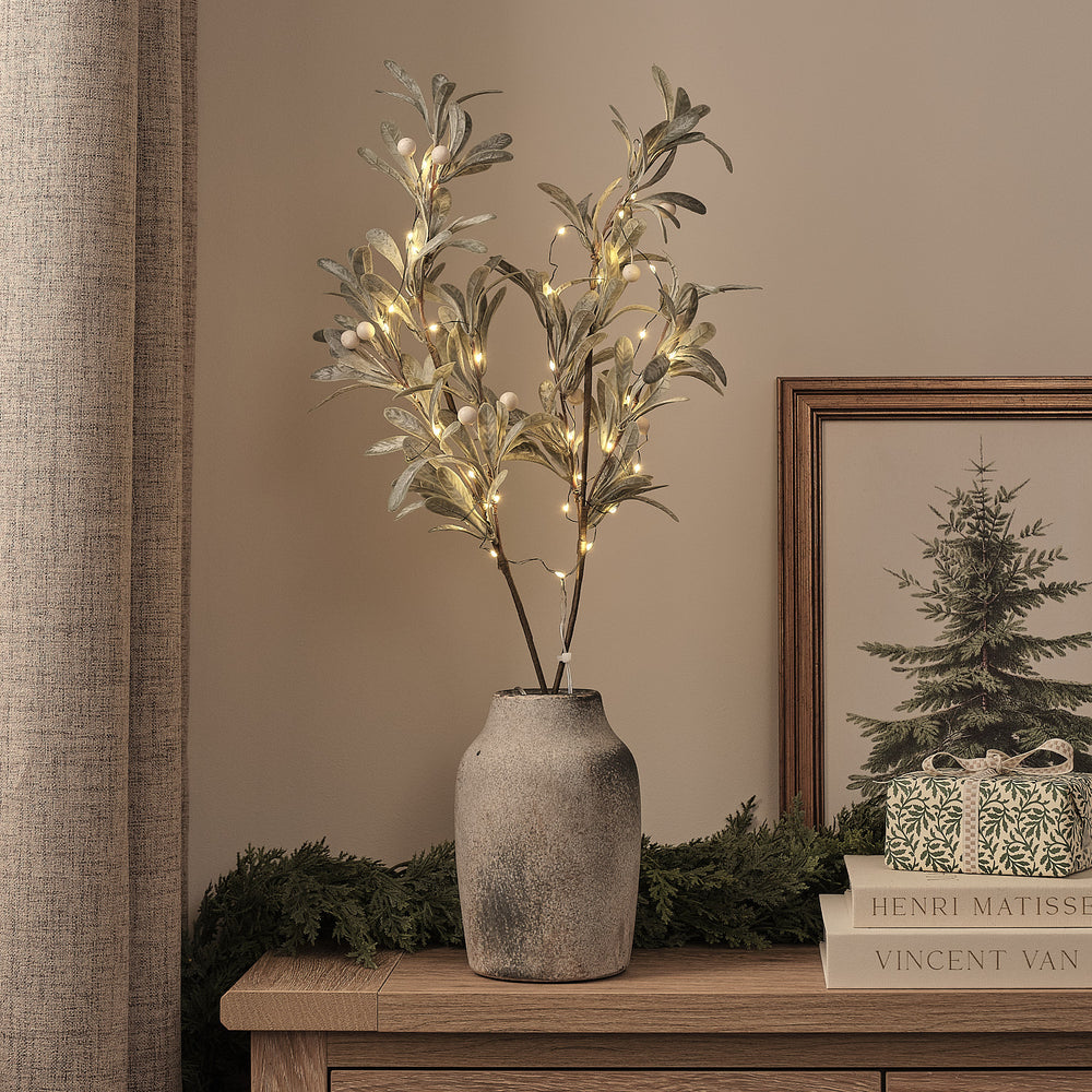 Beleuchtete künstliche Mistelzweige mit warmweißen LEDs in grauer Vase auf Holztisch