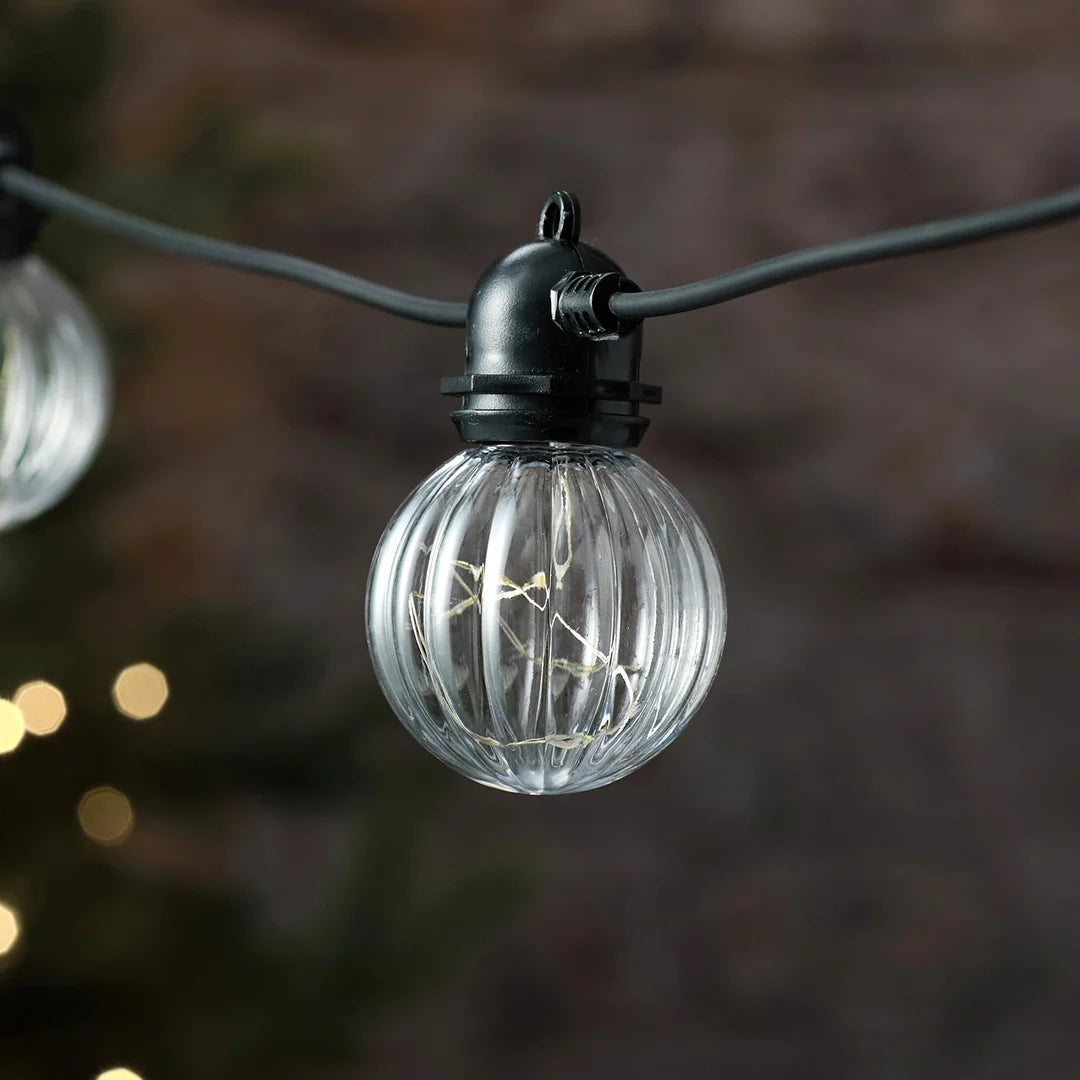 Detailansicht einer silbernen LED-Glühbirne mit Strukturmuster vor Tannenzweig.