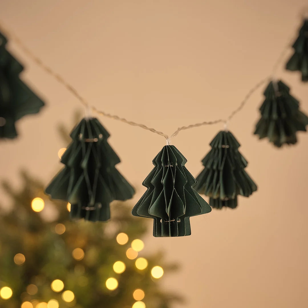 Lichterkette mit mehreren grünen Papier-Tannenbaum-Anhängern vor Lichterglanz.