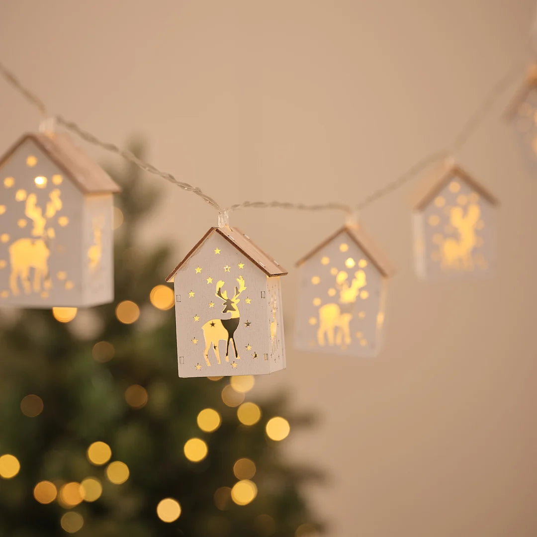 Lichterkette mit Häuschen-Anhängern mit Rentiermotiv vor Weihnachtsbaum und Lichterglanz.