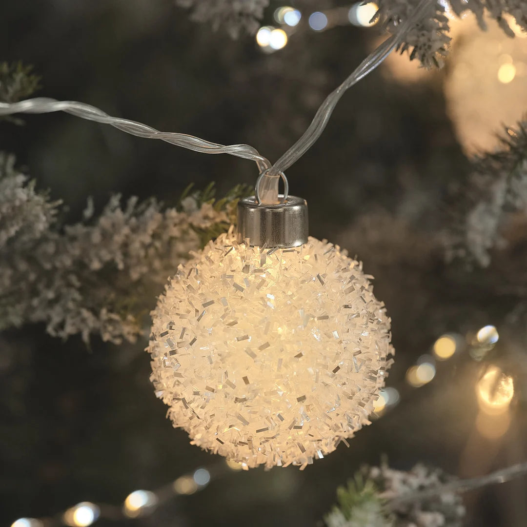 Strukturierte LED-Kugel an bereiftem Tannenzweig.