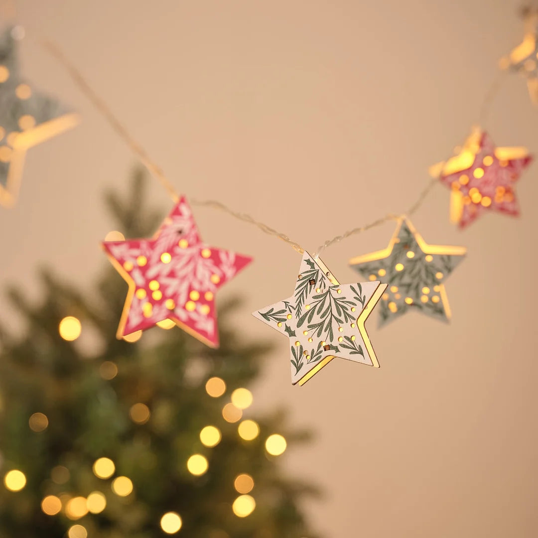 Lichterkette mit sternförmigen Papier-Anhängern in Rot und Grün mit Blattmuster vor Weihnachtsbaum.
