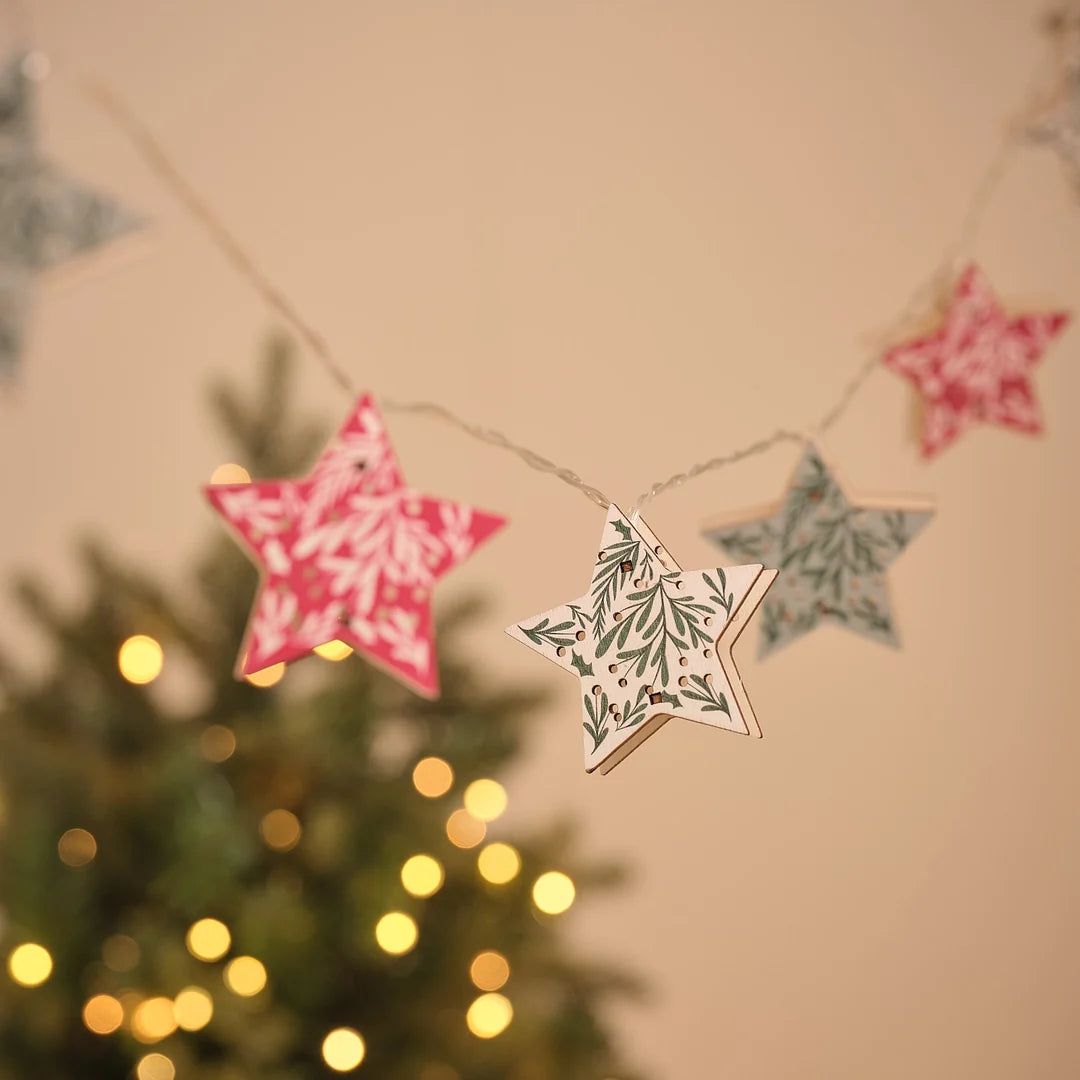 Lichterkette mit mehreren sternförmigen Papier-Anhängern in Rot und Grün vor Tannengrün.