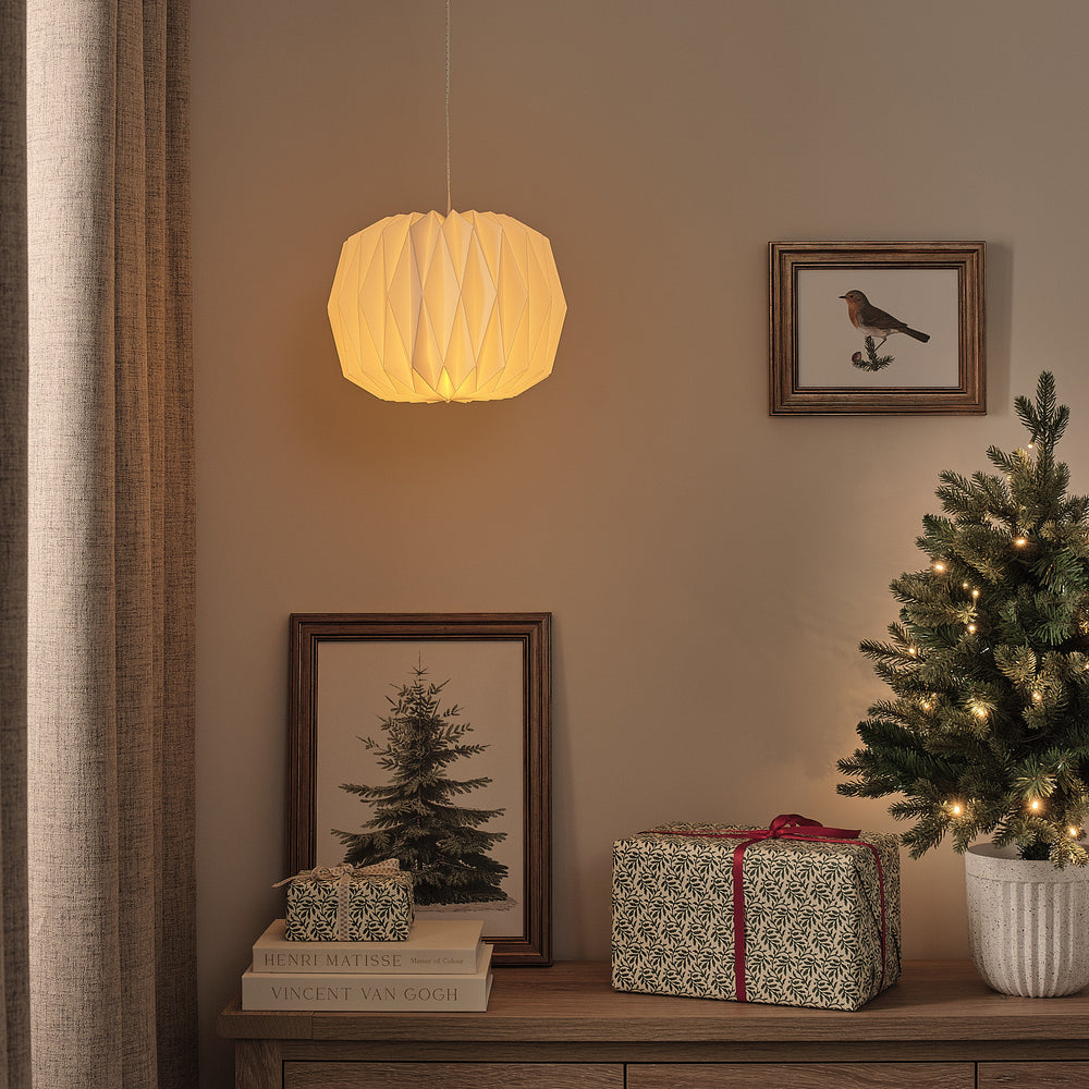 Hängende weiße LED-Papierlaterne mit warmweißem Licht neben Weihnachtsbaum und Geschenken