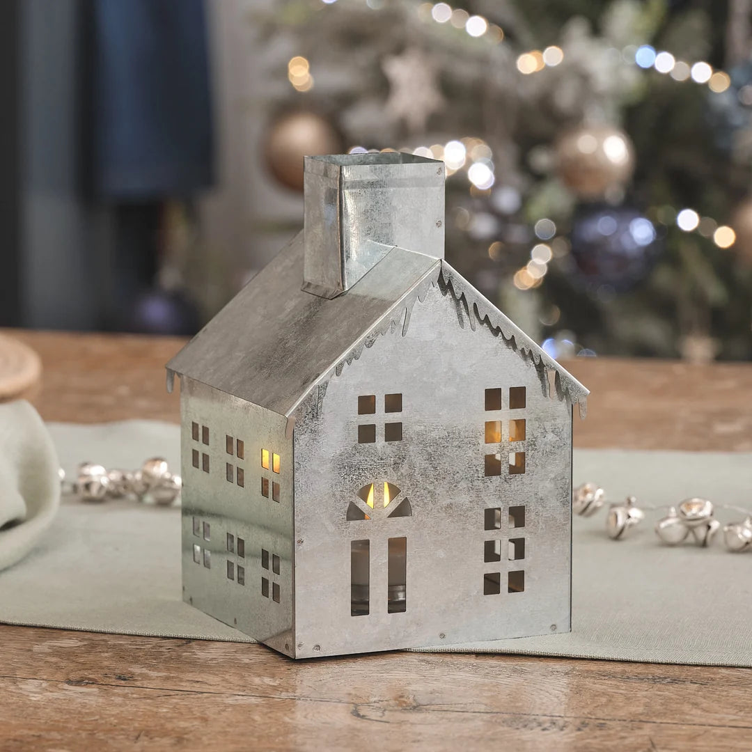 Porzellan-Weihnachtshaus mit warmweißen LED-Fensterlichtern, positioniert auf natürlichem Holzuntergrund mit cremefarbenen Dekoelementen und eleganten Weihnachtsakzenten – dekorative LED-Hausform für Tischdisplays, Kamindekoration und klassische Advents-Arrangements.