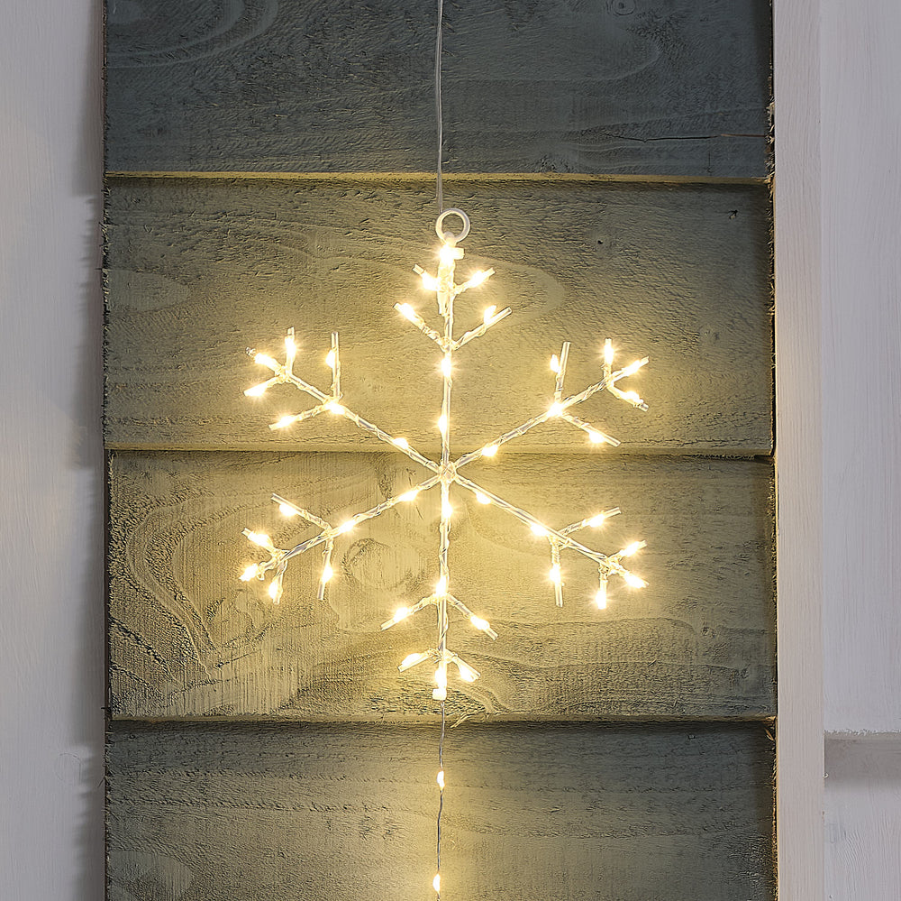 Nahaufnahme einer warmweiß leuchtenden LED-Schneeflocke an einer grauen Holzfassade