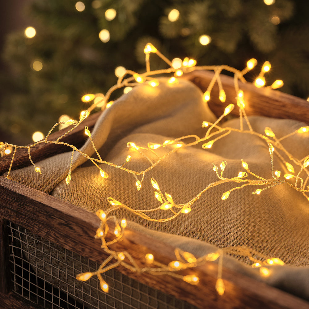 Goldene LED-Cluster-Lichterkette mit warmweißen Mikro-LEDs auf Stoff in Holzkiste