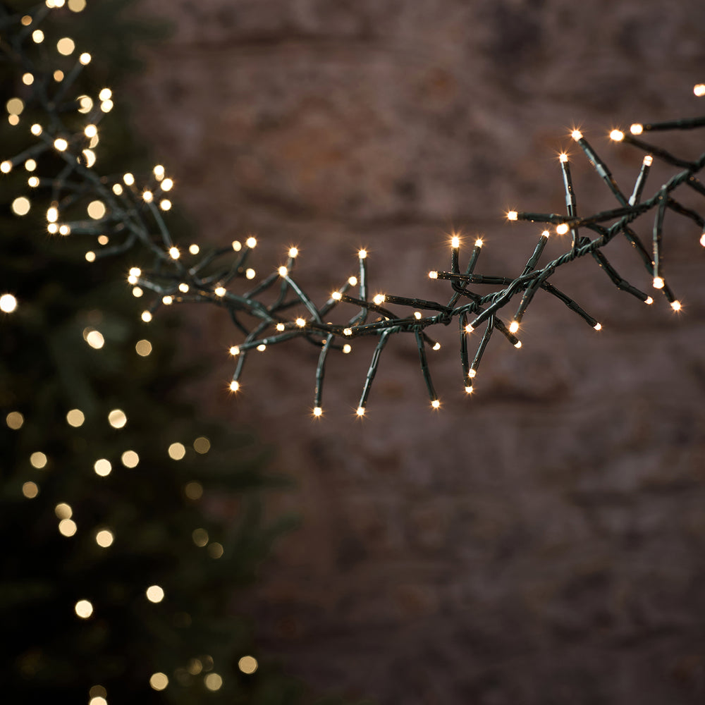 LED-Cluster-Lichterkette mit warmweißen LEDs an grünem Kabel leuchtend vor unscharfem Hintergrund