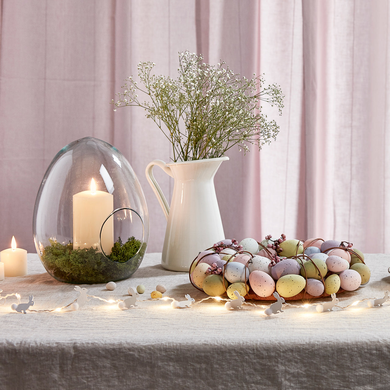 Osterliche Tischdeko mit Kranz und Osterei Vase vor rosafarbenem Vorhang.