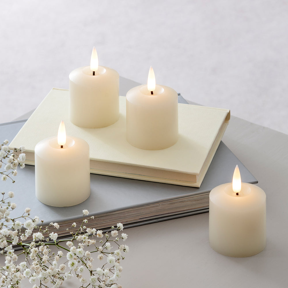 4 weiße LED-Kerzen aus Echtwachs auf einer weißen Tischdeko.