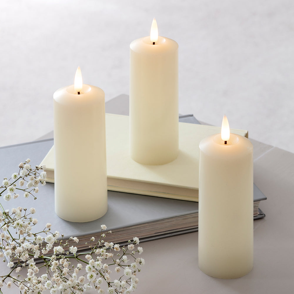 Drei LED-Kerzen stehen angeschaltet auf einem weißen Tisch.