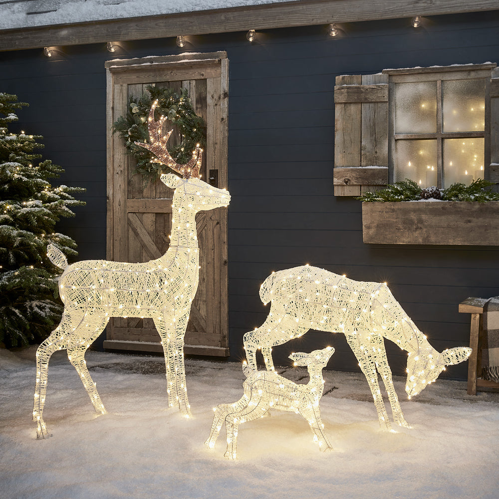 Drei weiße LED Rentier-Figuren mit Schleifen im Schnee vor Fenster und Holztür