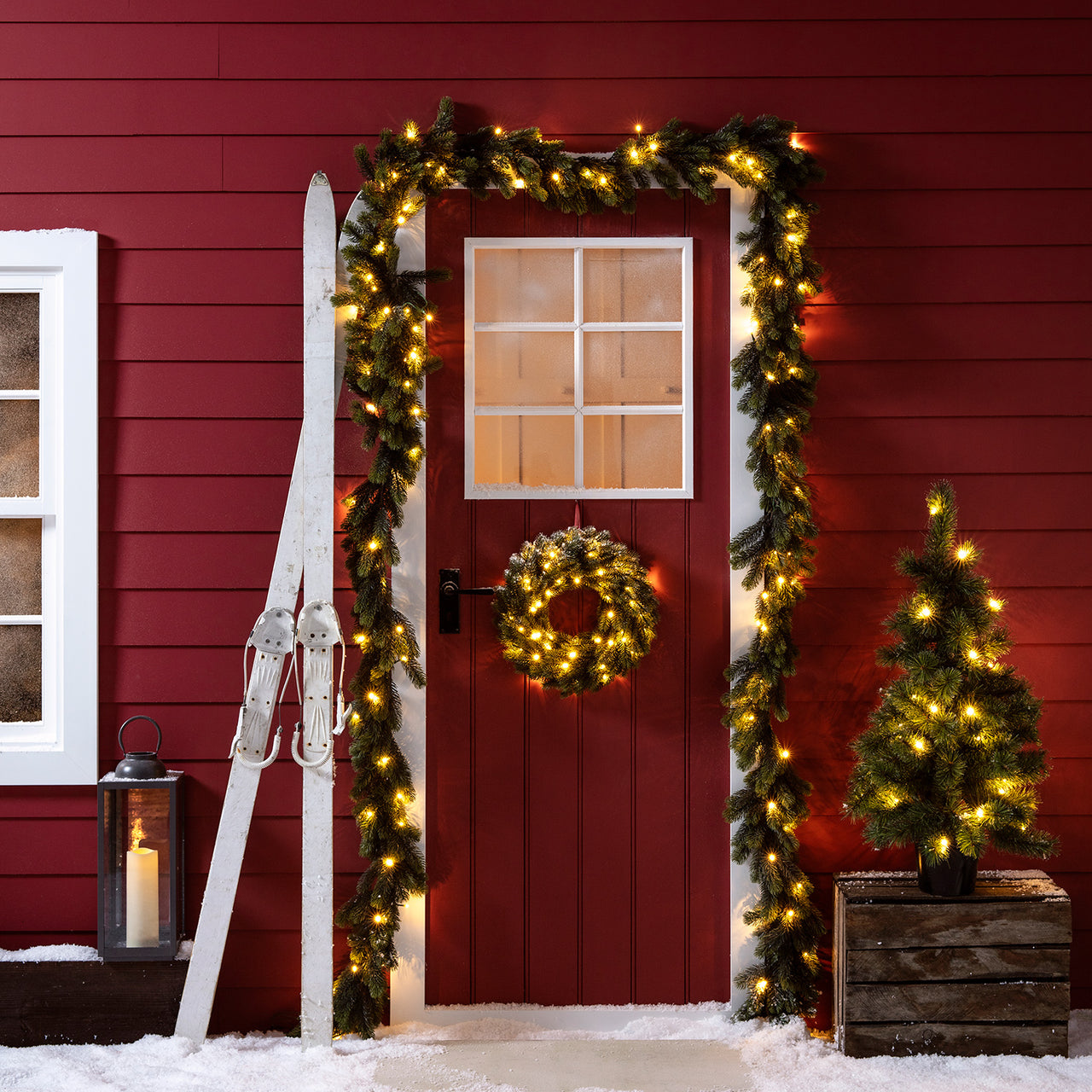 Weihnachtsgirlande und Kranz an Haustür mit LED-Laterne.