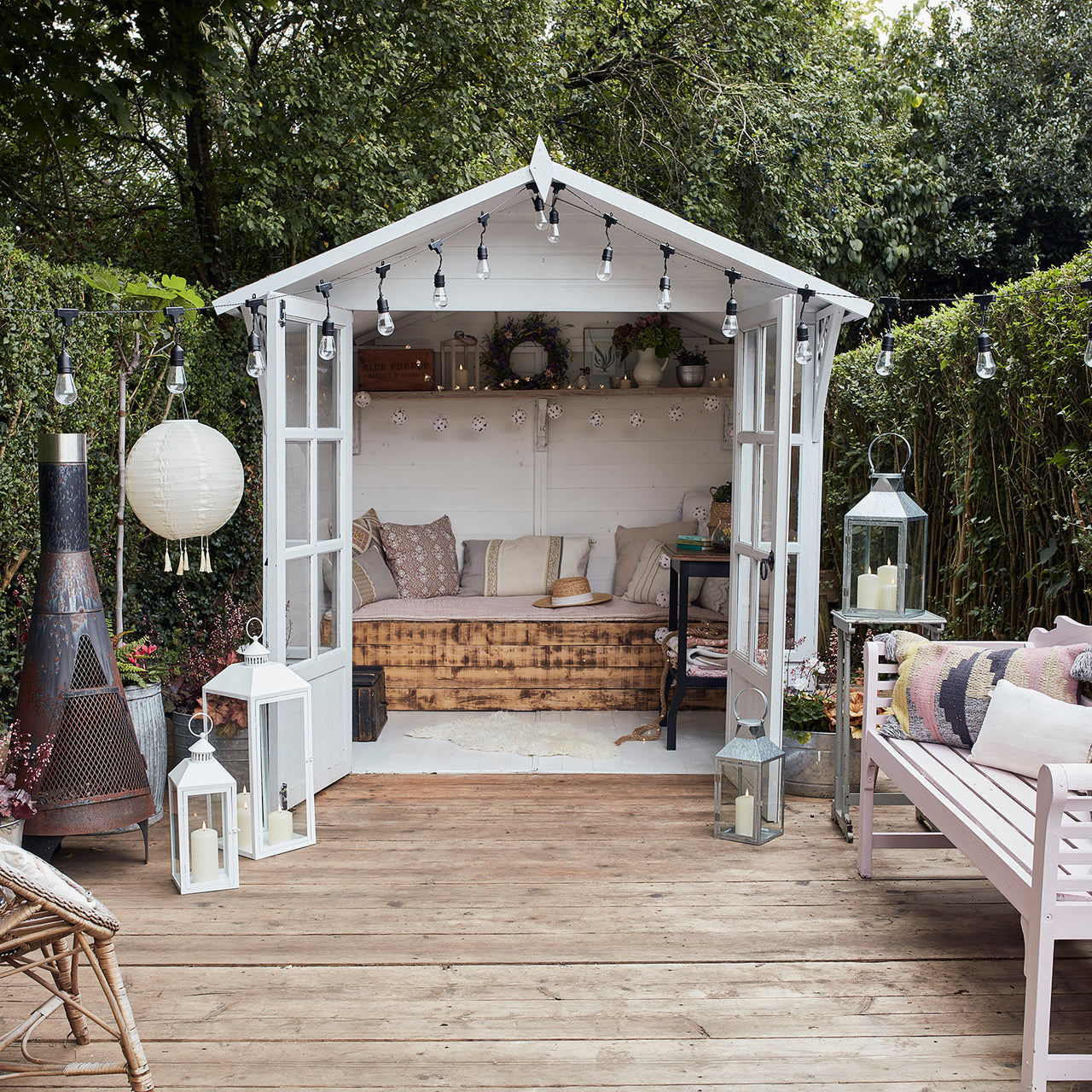 Weißes Gartenhaus mit Holzboden Terrasse, Sitzbank, Laternen und Lampions.