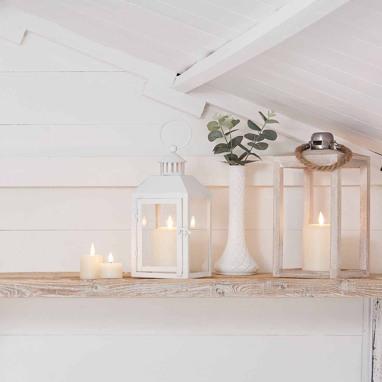 Holzregal vor weißer Wand mit LED Kerzen, Blumenvase und weißer Laterne.