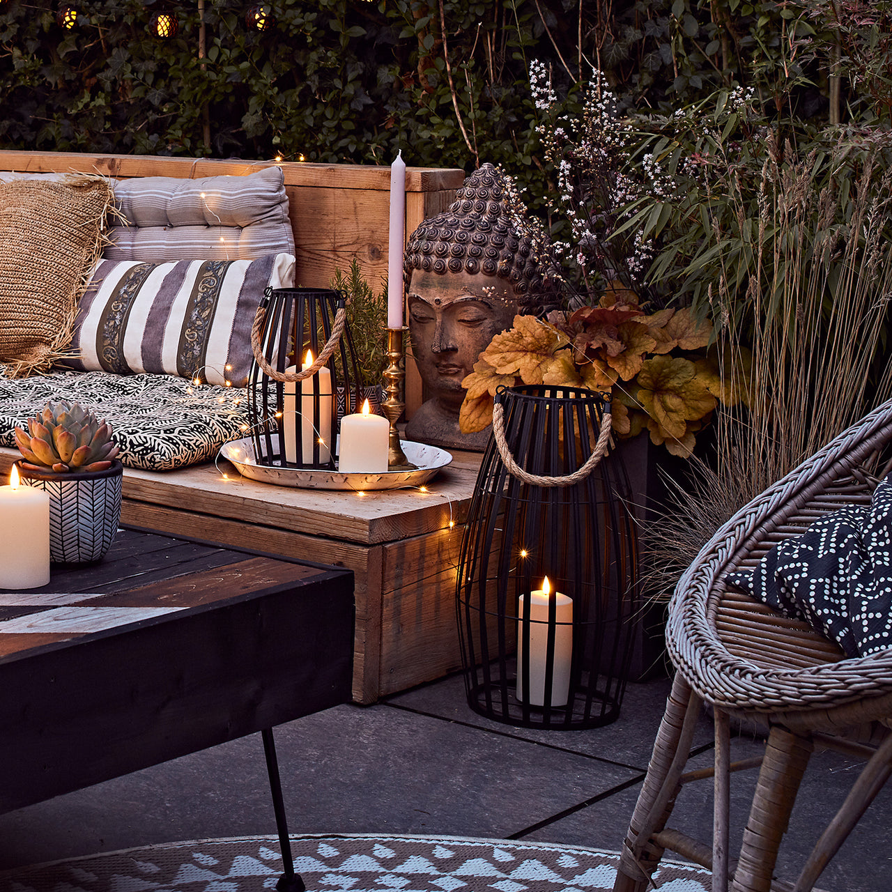 Terrasse mit gemütlicher Leuchtdeko und Sitzbank mit Kissen, Kerze und Pflanzen.