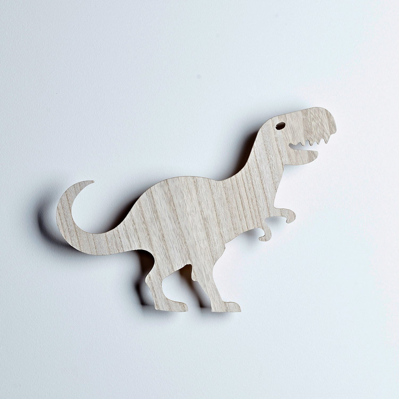 Ausgeschaltete T-Rex Wandlampe vor weißer Wand aus Holz.
