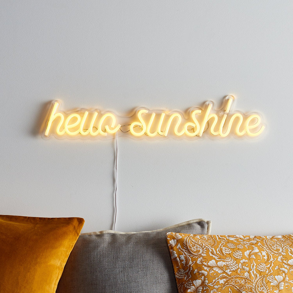 Gelbe Neonschrift hello sunshine an weißer Wand mit Kabel und Kissen.