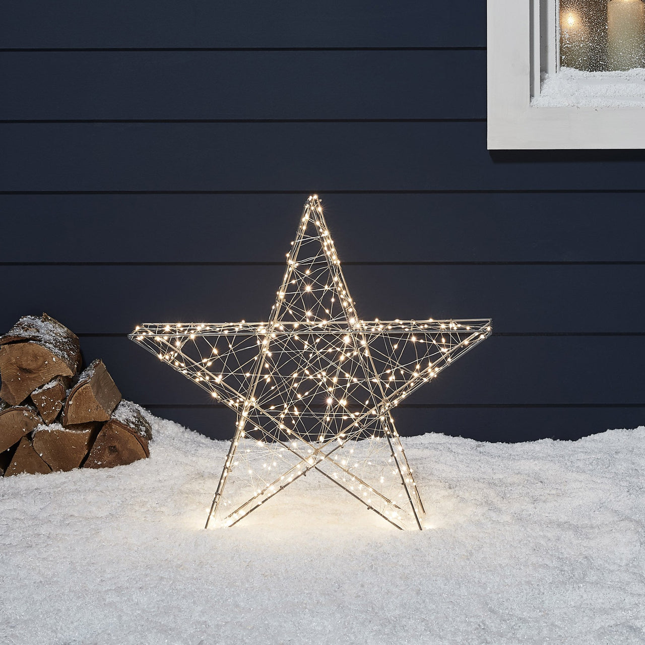 Mittelgroßer LED-Stern im Schnee vor blauer Hauswand.